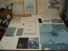 work table with text works 'mitten, midden, mire mirth' and Ci/SfB sculpture, text work 'The Devil is in the Detail'