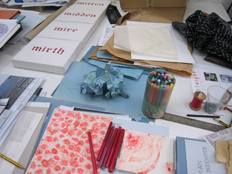 work table with Ci/SfB sculpture, 'Mitten, Midden, Mire, Mirth' text work, drawing in red ink on paper.